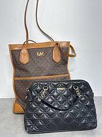 Front view of both handbags side by side showing Michael Kors brown tote with tan leather and black quilted Kate Spade handbag with chain handles.