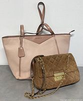 Two Michael Kors bags together, large blush pink leather tote with a medium brown suede quilted shoulder bag.