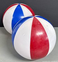 Two spherical glass light shades with alternating red, blue, and white panels, resembling beach balls, placed side by side on a flat surface against a dark backdrop.