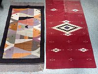 Photo showing two handwoven kilim rugs side by side on floor, one red with geometric diamond pattern, one multicolored with bird motifs and dark border.