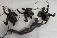 Four dark resin sculptures of male climbers each attached to wire loops for hanging, displayed on a flat white surface.