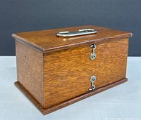 Wooden oak box with metal handle and dual keyhole locks on front, closed.