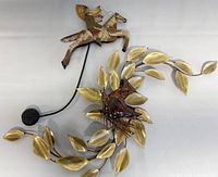 Photo showing two copper and brass wall sculptures, one of a horse and rider, and another of a cat head surrounded by brass leaves.