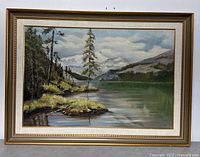 Frontal image of the framed landscape painting showing a lake, trees, and snowy mountains with cloudy sky. The frame is gold and brown wood.