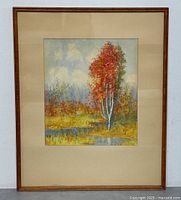 Full view of the framed vintage landscape painting depicting red-leafed tree and water with matting and wooden frame.