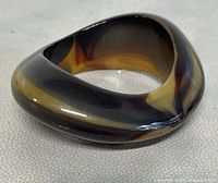 Close-up side profile view of the asymmetric faux tortoise shell bangle bracelet, showing glossy finish and color gradients from amber to black.