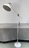 Front and side views of the white IKEA adjustable floor lamp with brass joints, round base, and white cord.