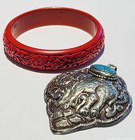 Photo showing both the red cinnabar bangle and the large elephant pendant with turquoise accent lying next to each other on white background.