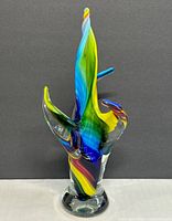 Front view of the colorful MCM hand blown glass sculpture showing the full height and vibrant colors in a studio setting with a dark gray backdrop.