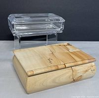 Front and angled view of clear rectangular glass box with beveled edges on display stand behind onyx stone box with natural light brown patterning and smooth finish.