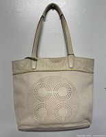 Full view of beige COACH designer tote bag with perforated logo pattern and leather handles