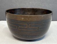 Side view of dark metal meditation singing bowl showing geometric engravings on the exterior wall.