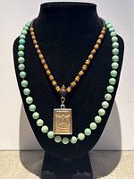 Front view of two necklaces on display bust, showing Buddha pendant on brown and black bead necklace and mint green round bead necklace.