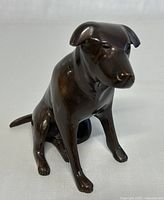 Front-left angled view of the cast brass/bronze Labrador dog figurine showing the seated pose and smooth dark patina finish.