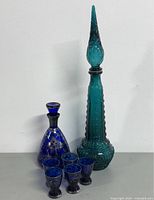 Two glass decanters and five shot glasses displayed against a white wall.