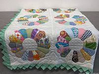 Close-up photo showing detailed multicolor fabric petals sewn in the traditional Dresden Plate pattern, white quilted background and scalloped green binding.