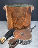 Front view of large copper bucket with fireplace bellows and brush placed in front.