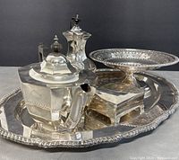 Set of vintage silver plated items displayed on the serving tray including teapot, coffee pot, rectangular box, and pedestal compote.