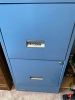 Front view of blue metal filing cabinet showing two drawers, lower drawer with lock and metal handles, SteelWorks brand nameplate visible on upper drawer.