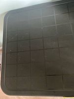 Top surface of the black plastic table top showing grid texture.