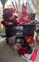 Full view of lot with Canadian flag pillows, hats, fanny packs, plastic Canadian flags, and board game on cabinet.