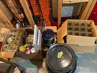 Boxes containing multiple glass canning jars of various sizes, metal lids, and assorted canning utensils and accessories. Black speckled enamel canning pots with lids visible in front.