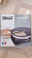 Box of Tibos electric crepe maker showing front and product image including crepe and wooden spreader.