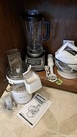 Overview photo of all four appliances on a wooden shelf and countertop including blender, hand mixer, hand blender, and food processor with manual.