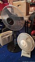 Photo showing black Canarm pedestal fan, white Heaven Fresh small fan, and white Honeywell air purifier on blue carpet.