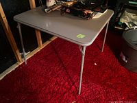 Overview of the gray rectangular folding table standing on a red carpet with some items on top.