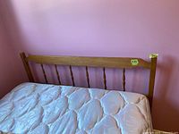 Wooden bed frame headboard with spindle design and attached mattress.