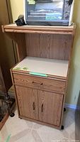 Wood kitchen cart microwave stand holding a toaster oven with visible cabinet and shelf structure.