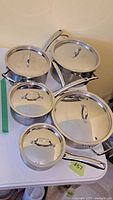 Full set of five Lagostina Hotel-Pro stainless steel pots with lids displayed on table. Sizes range from small to large with matching lids and handles visible.