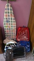 Ironing board cover with floral and checkered pattern next to plastic hangers and pop-up laundry hampers packed in cloth bags