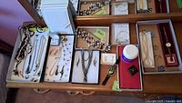 Overview of jewelry and watch lot showing multiple trays with necklaces, rings, earrings, and watches including jewelry box on wooden dresser