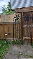 Full view of two solar garden stake lights with glass material plus decorative flower stakes and metal hook stake.