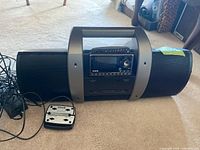 Full view of Sirius SUBX1C satellite radio boombox showing front console with screen and buttons, speakers on either side, and power cable attached.