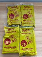 Four sealed packs of Mac's garbage bags on table