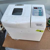 Front and top view of the white Black & Decker All-In-One Plus Automatic Breadmaker showing the control panel with buttons and viewing window on lid. Visible dirt and wear marks on surface.