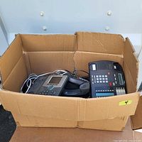 Box containing four assorted business telephones with wired handsets, black and gray, seen from above.