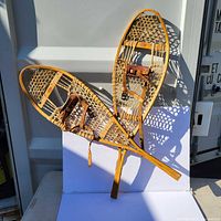 Pair of vintage wooden snowshoes with rawhide webbing and leather bindings, photographed side by side against a white background to show overall condition and design.