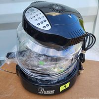 Full view of NuWave Oven Pro showing digital control panel on black plastic top, clear glass cooking bowl, with power cord coiled beside it.