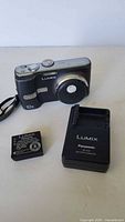 Panasonic Lumix DMC-TZ1 camera with battery and charger laid out on a flat surface.
