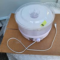 Full view of the white Salton VitaPro food dehydrator showing five transparent stackable trays and the power cord, placed on cardboard.
