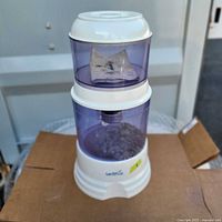Full view of Santevia alkaline gravity water filtration system with stacked translucent purple chambers and white base on cardboard.