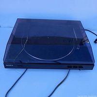 Front view of Sony turntable with transparent smoke plastic dust cover showing its cracked condition and attached power cord.