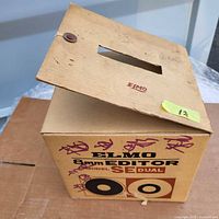 Original cardboard box and top cover for the Elmo 8mm film editor Model SE Dual with markings and some wear.