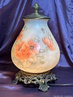 Front view of acorn-shaped glass lamp showing floral painting and metal base