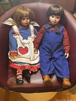 Full view of both 22" porcelain dolls seated in chair