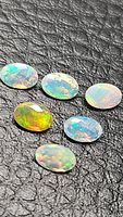 Six oval cut Ethiopian opal gemstones arranged on a black textured background, showing various multicolored rainbow flashes.